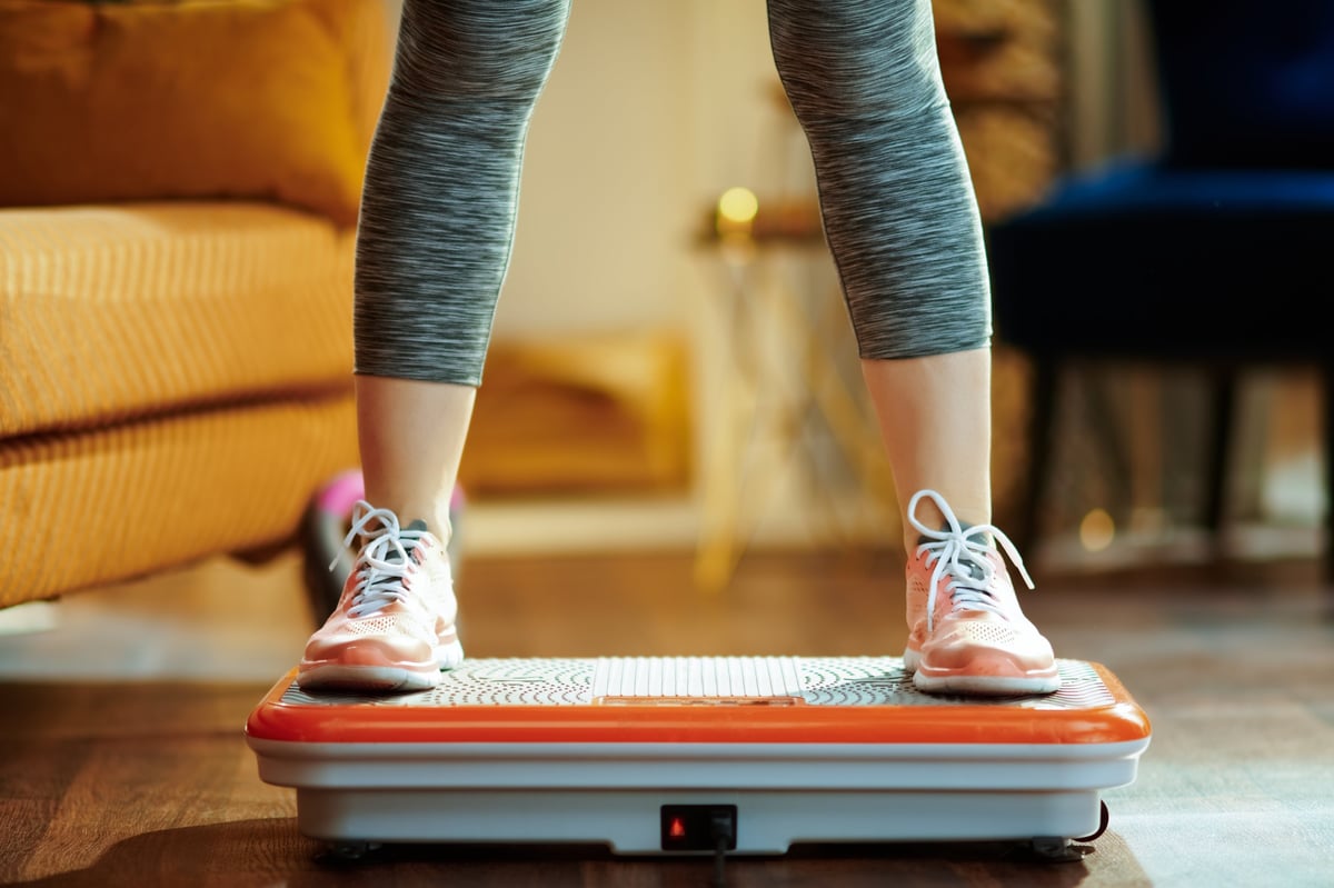 Closeup on young woman in fitness clothes in the modern house training using vibration power plate
