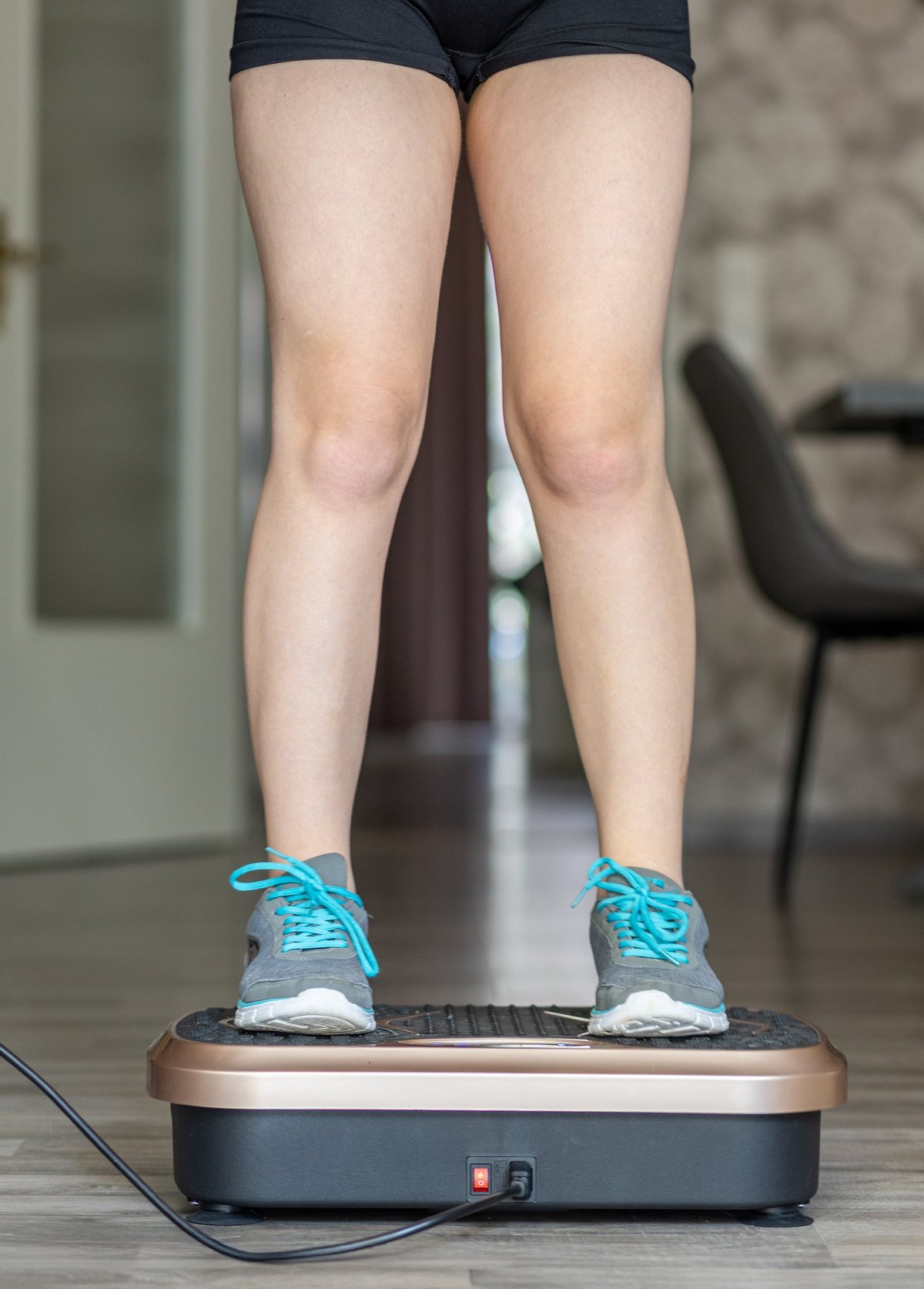 Woman stands on vibration plate machine in home environment, demonstrating fitness routine and equipment usage for health and wellness benefits