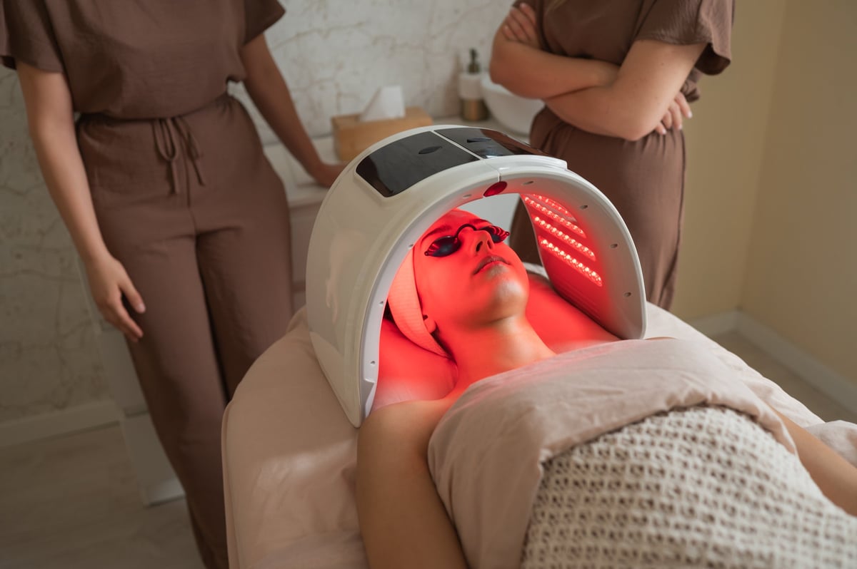 Young woman lying down receiving led light therapy by a professional at a wellness center