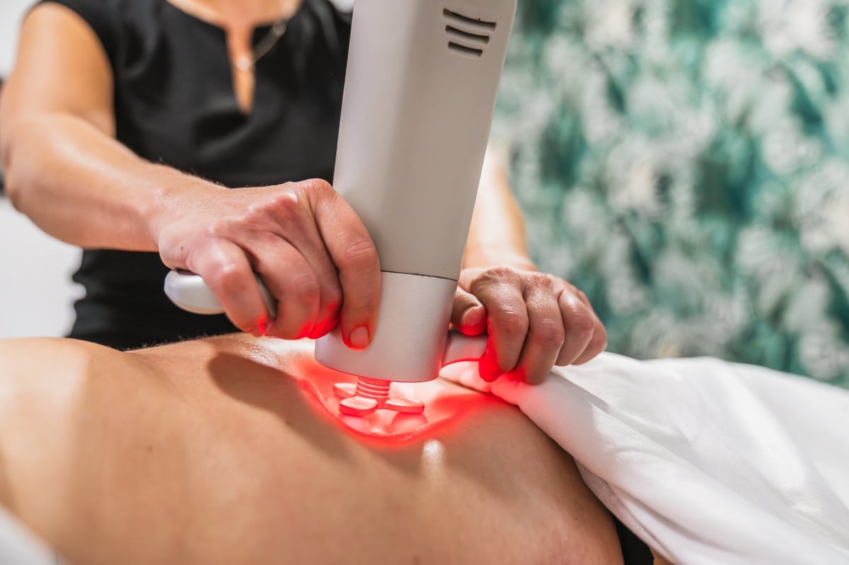 Experienced therapist using a deep physioactive massage system with rotating heads and red light, focusing on body wellness