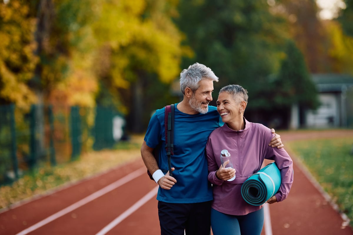Happy mature sports couple walking on running track while exercising at the park.