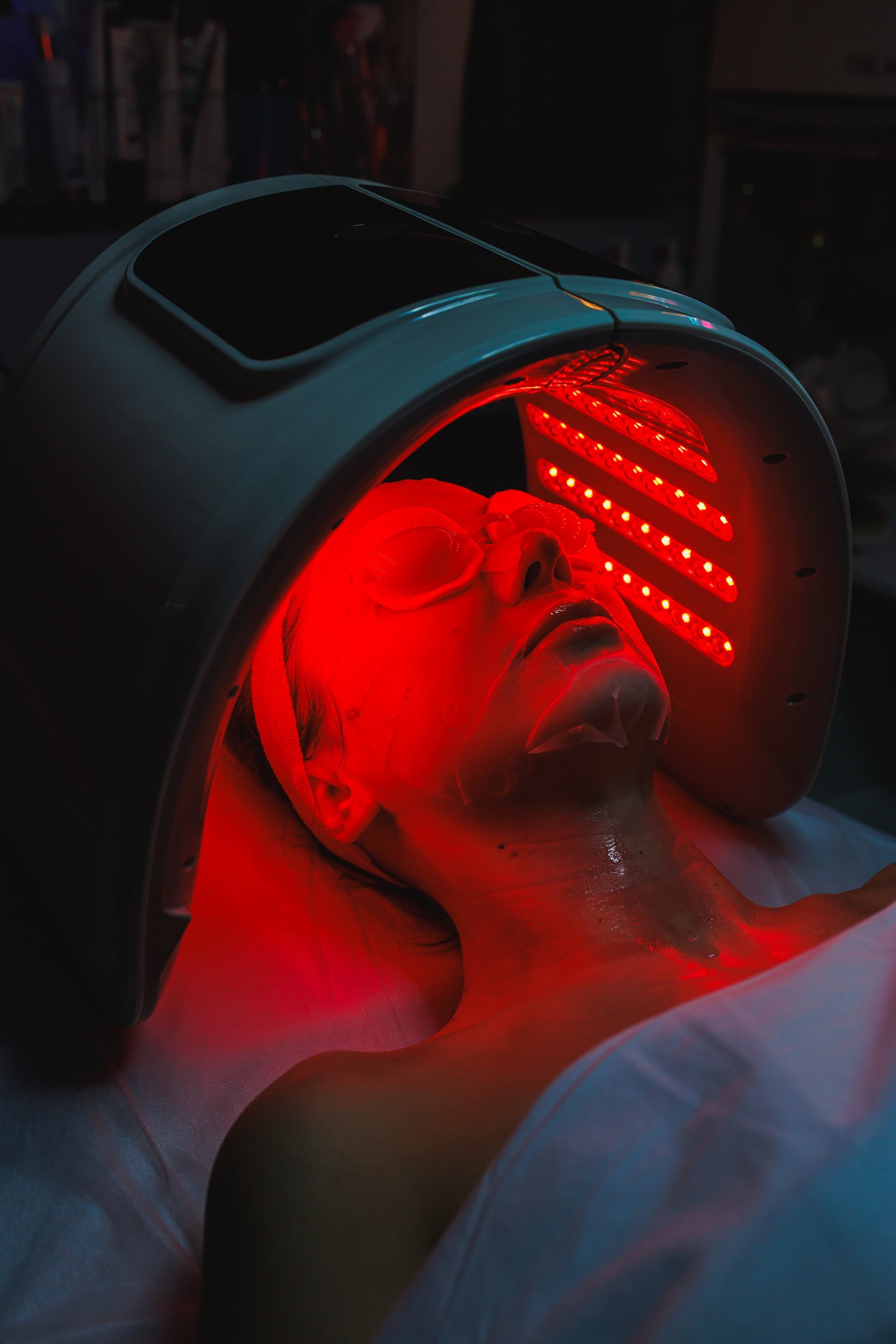 A woman is at her cosmetology appointment. She is receiving a red light therapy treatment. The salon has various skincare products around.