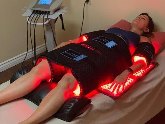 Patient receiving red light therapy treatment lying on bed with infrared LED pad and control device nearby