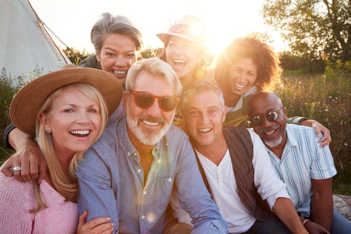 Group of six diverse friends smiling together outdoors during golden hour sunset in a rural garden setting